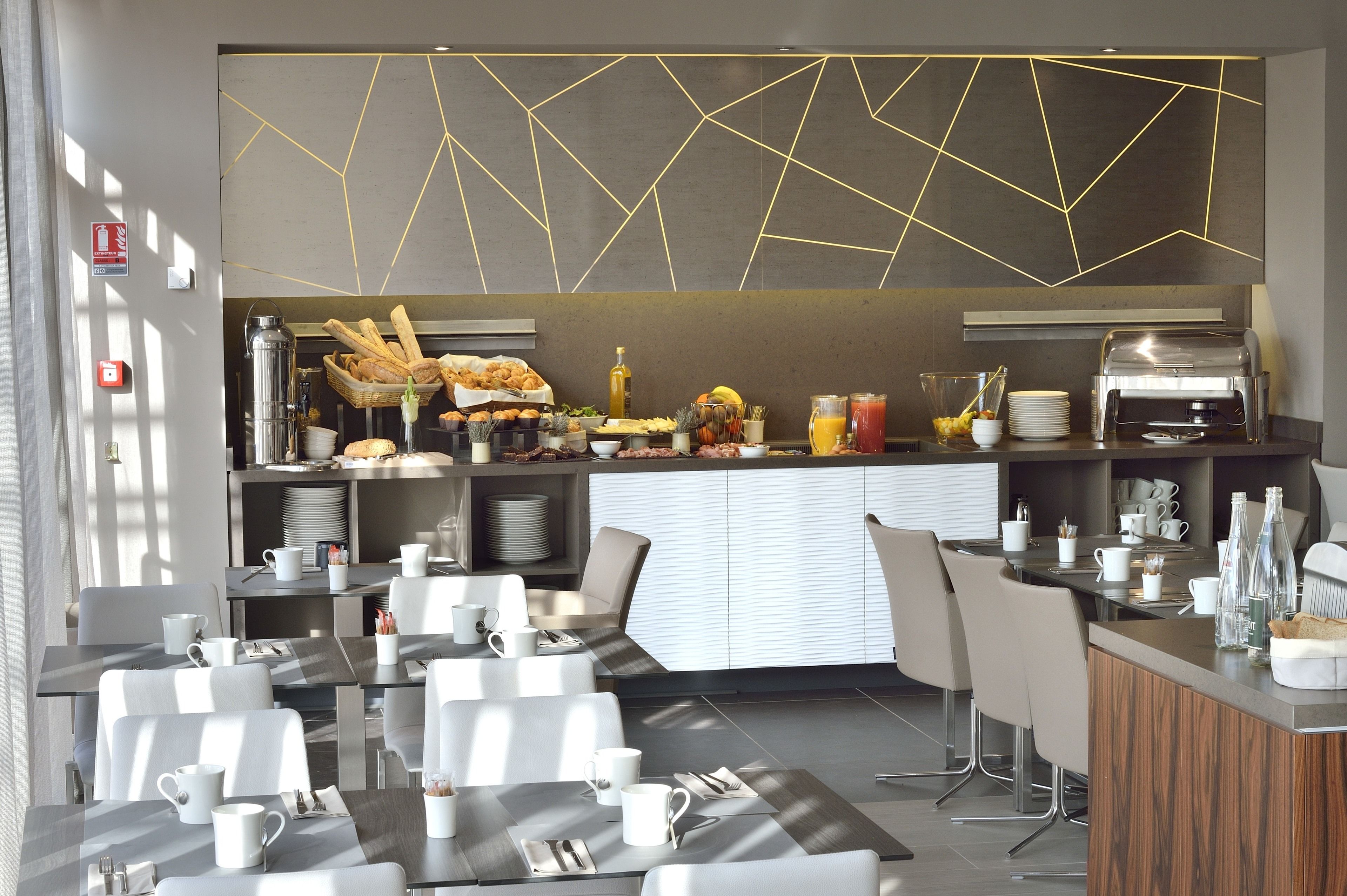 Un restaurante moderno con una barra central, sillas blancas y un diseño geométrico en el techo.