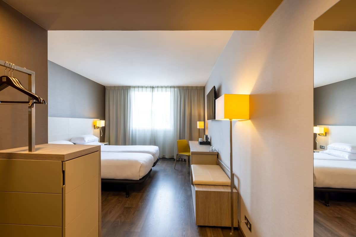 A hotel room with two beds, a desk, a chair, and a wardrobe.