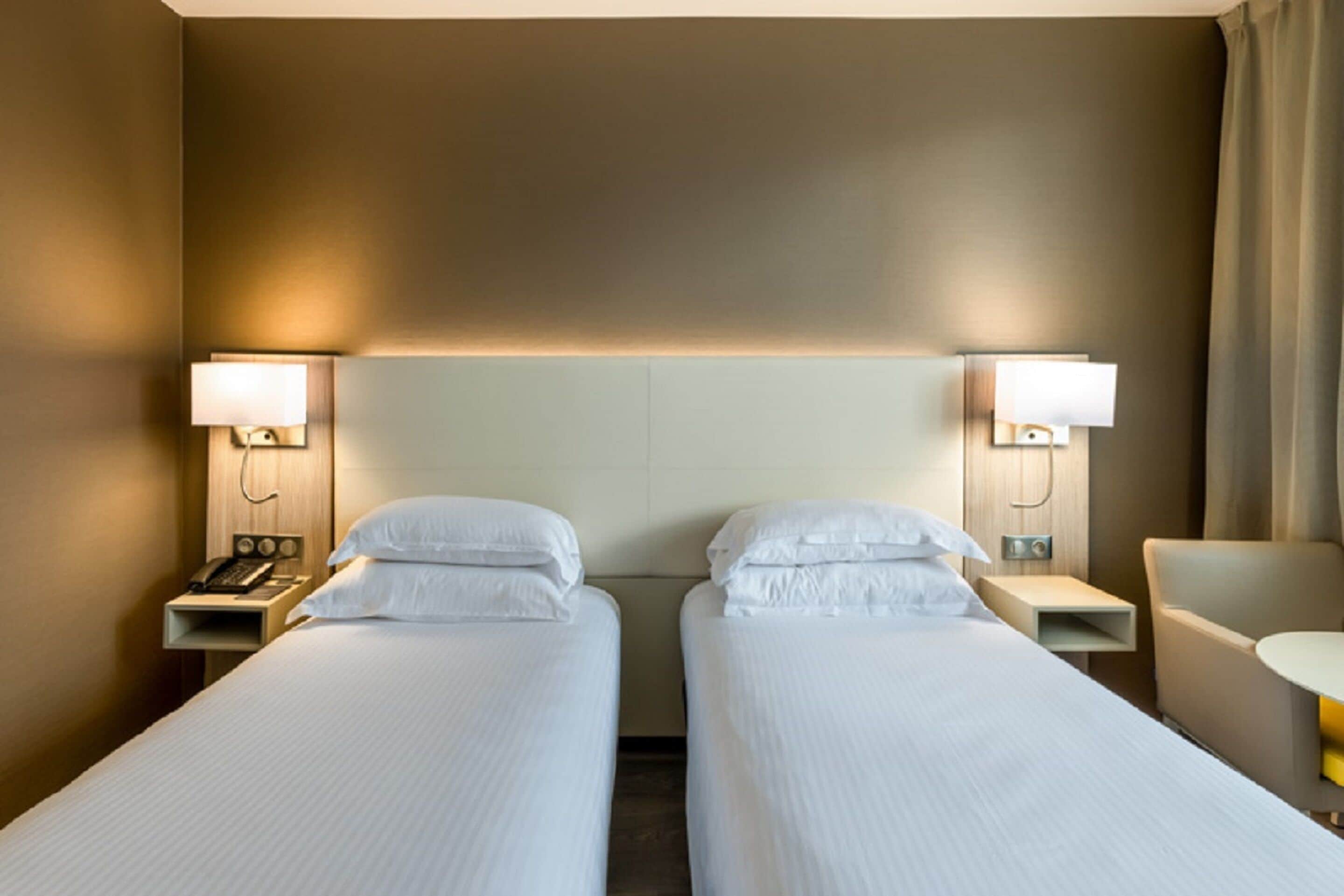 Een hotelkamer met twee enkele bedden, nachtlampjes, een kleine tafel en een stoel.