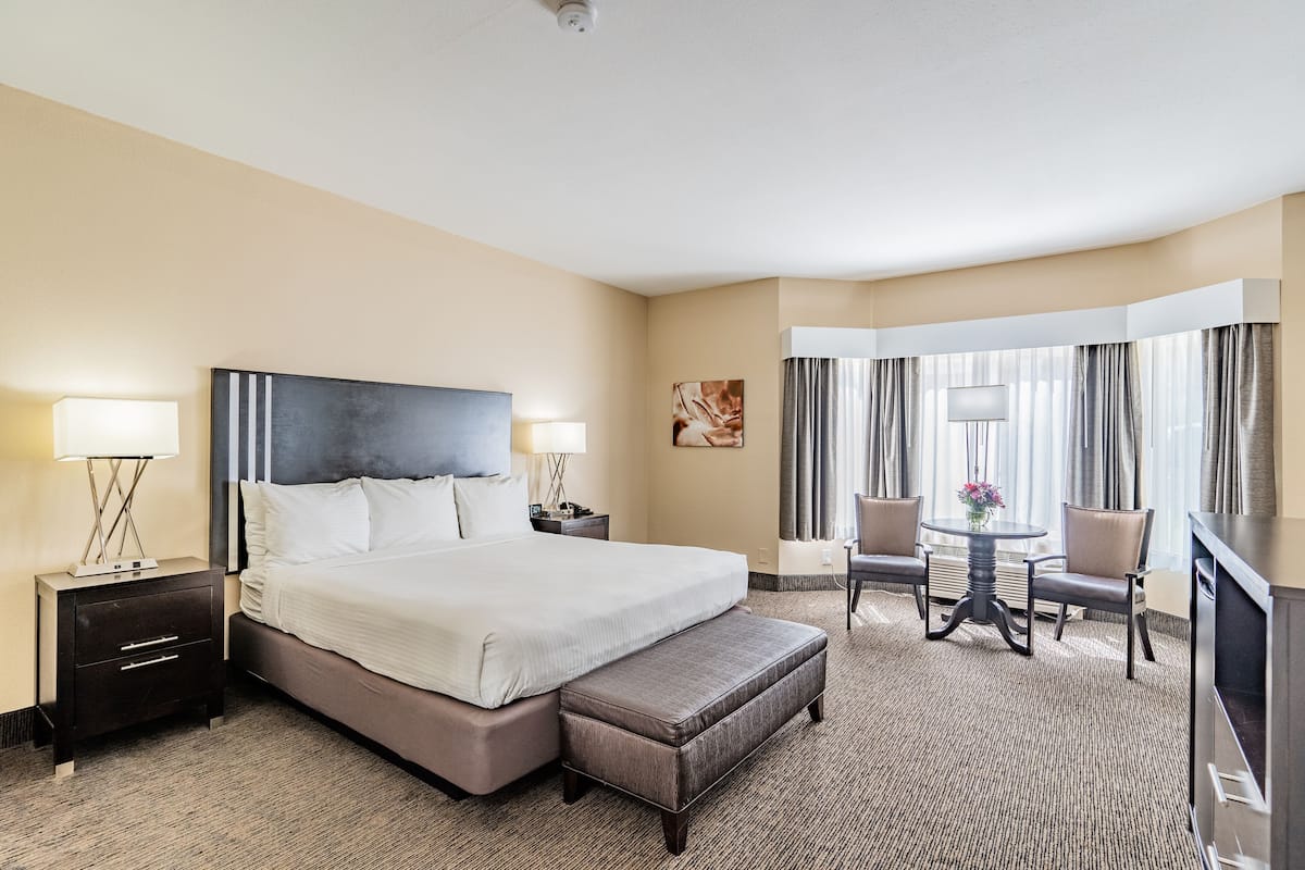 Une chambre d’hôtel avec un grand lit, un bureau avec une chaise, une télévision et une fenêtre avec des rideaux.