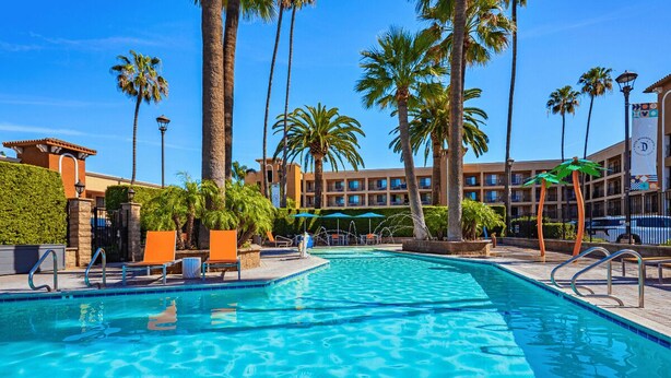 A swimming pool with lounge chairs, palm trees, and a building with multiple balconies in the background.