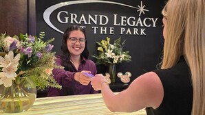 A reception desk with a sign reading 'Grand Legacy at the Park' and a woman handing a card to another person.
