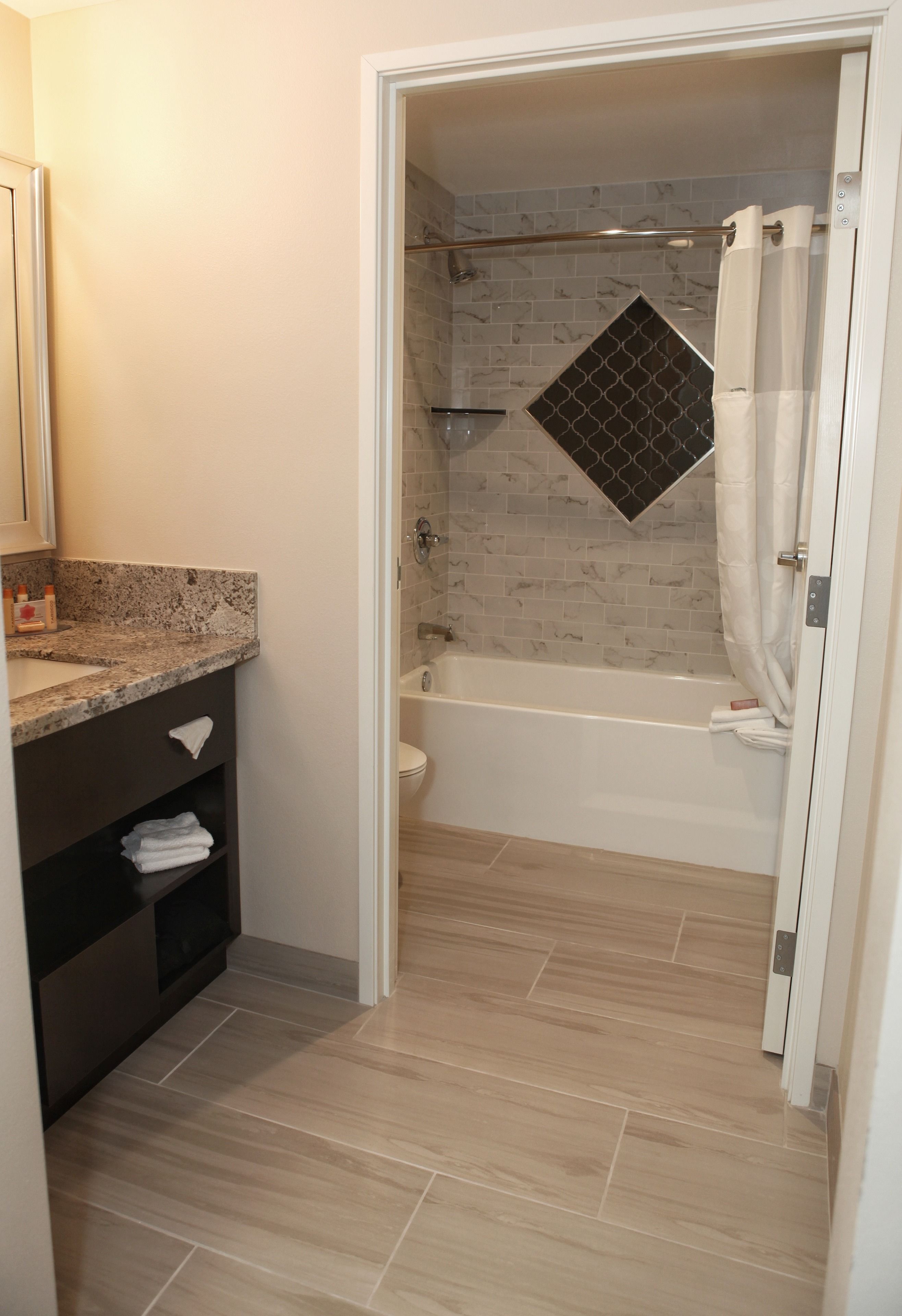 Un baño con ducha, bañera, pared de azulejos de mármol y encimera de granito.