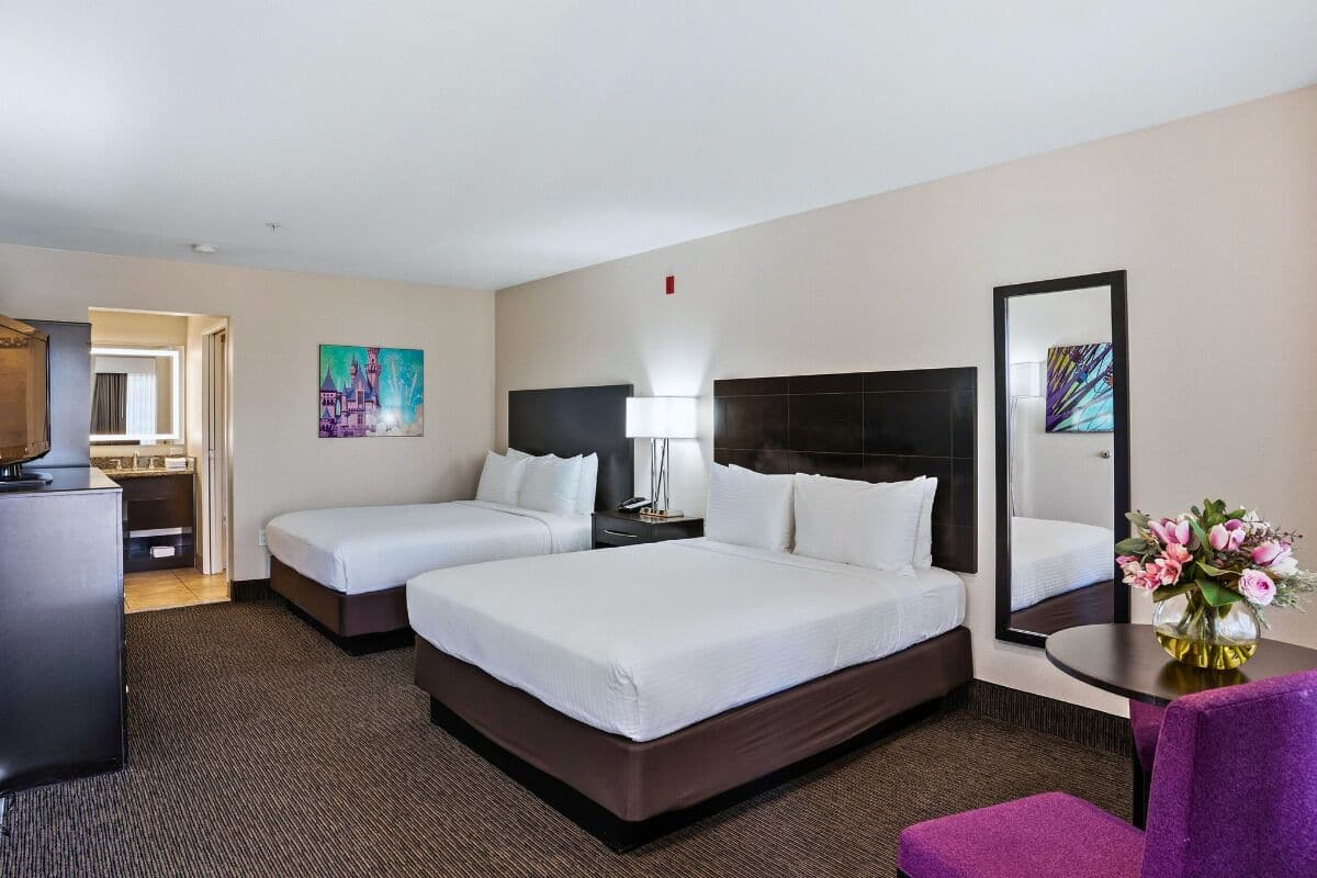 Ein Hotelzimmer mit zwei Betten, einem Schreibtisch, einem Sessel, einem Fernseher und Bildern an den Wänden.