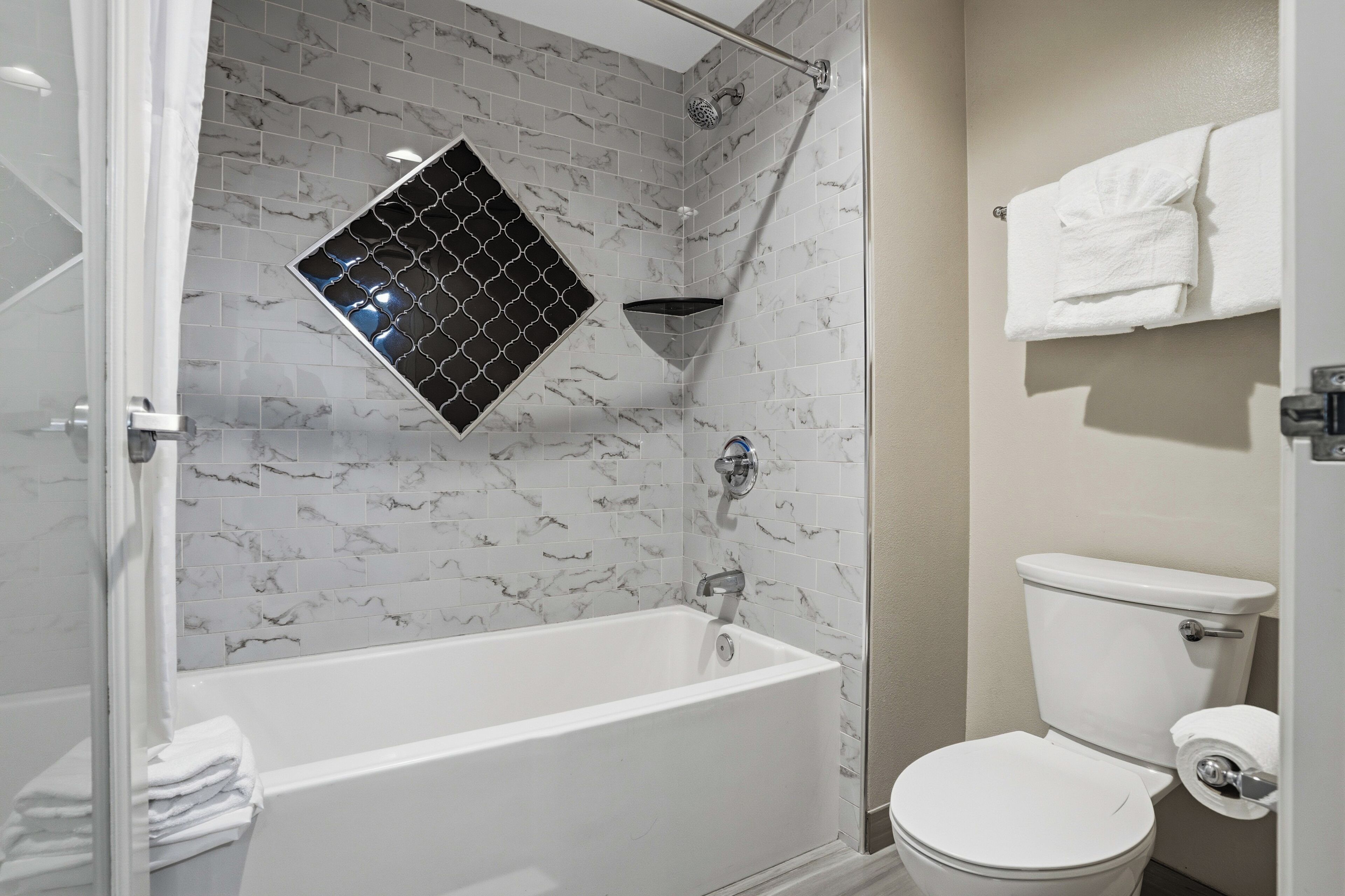 A bathroom with a white bathtub, a toilet, and a shower with a black and white patterned tile wall.