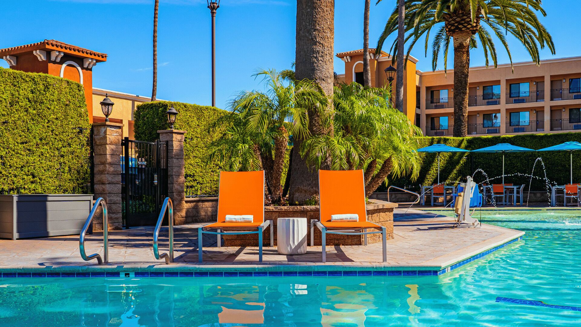 A pool area with lounge chairs, a palm tree, and a building with balconies.