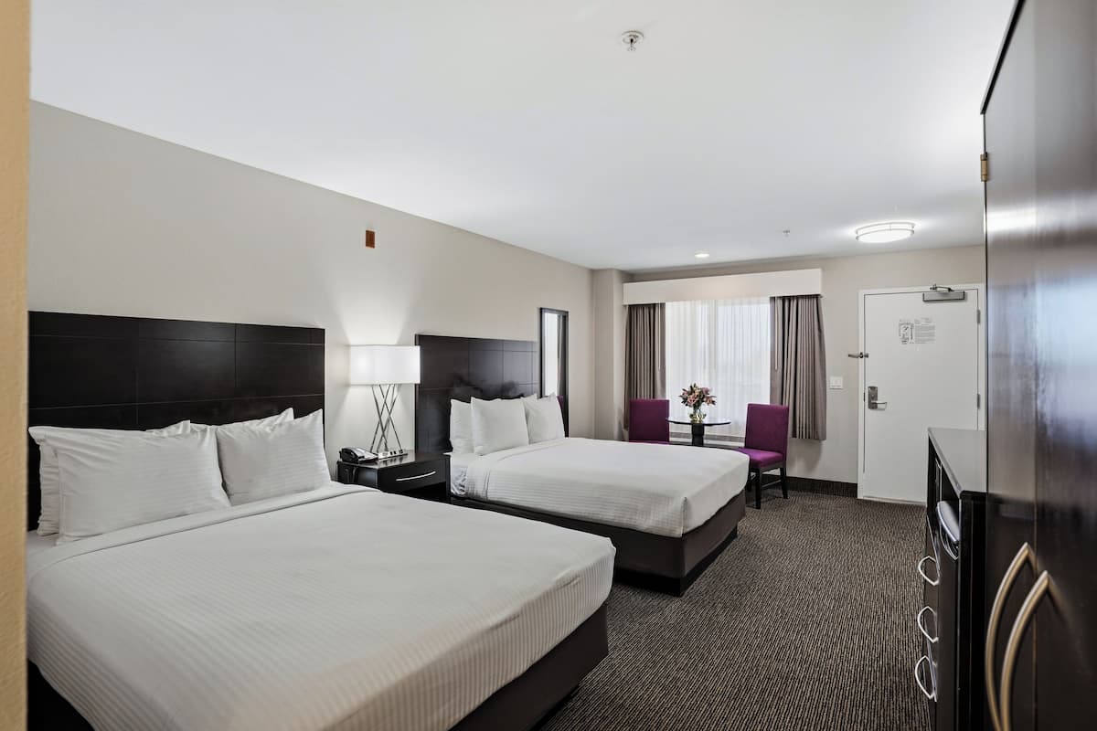 Une chambre d’hôtel avec deux lits, un bureau, une chaise, un réfrigérateur et une porte avec une pancarte.