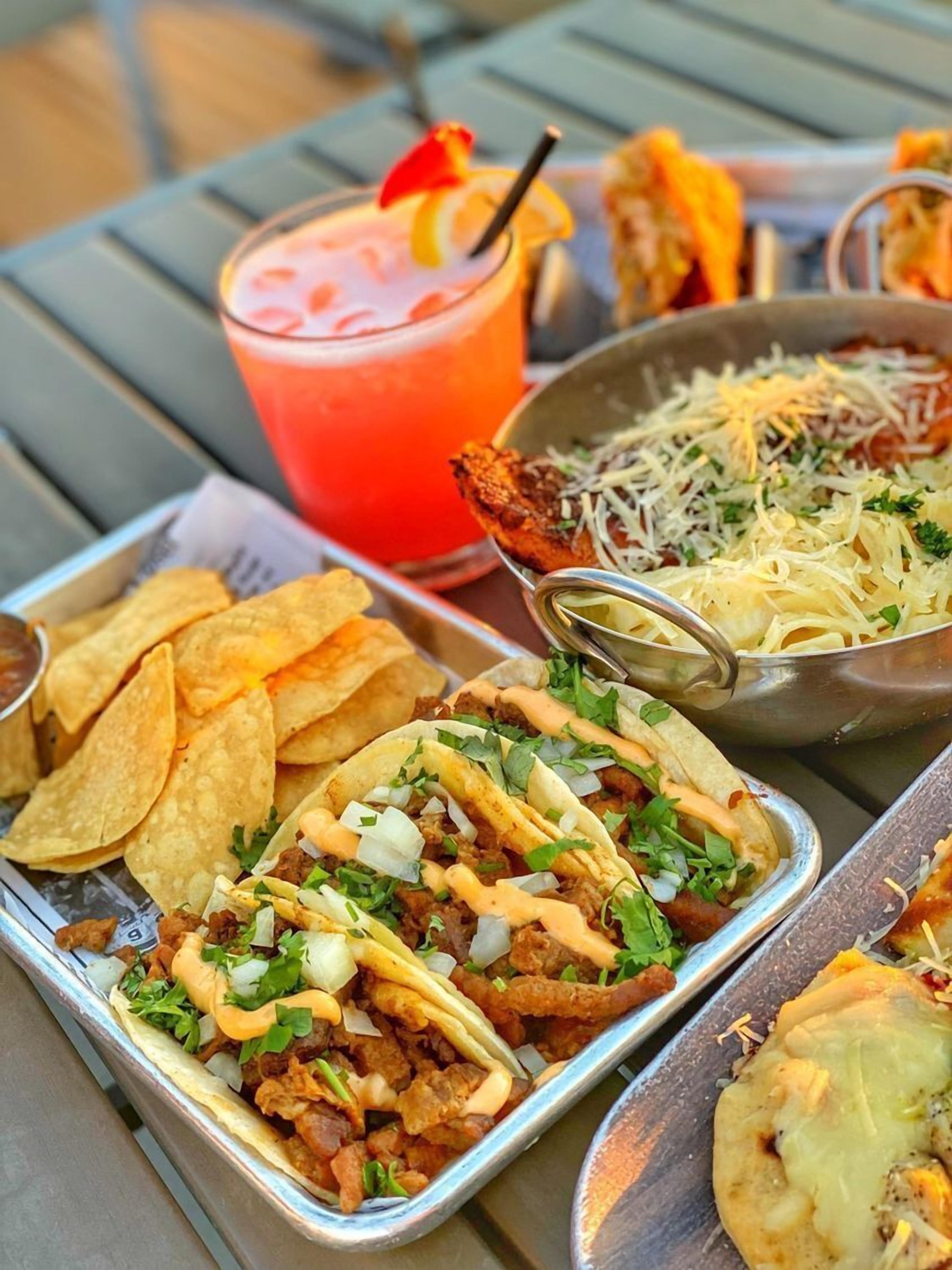 A meal with tacos, a drink, and a bowl of shredded cheese on a table.