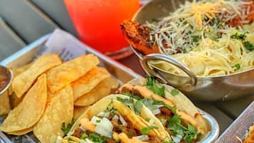 A meal with tacos, a drink, and a bowl of shredded cheese on a table.