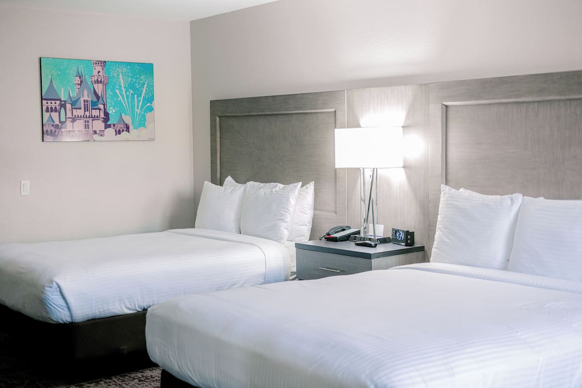 Ein Hotelzimmer mit zwei Betten, einem Nachttisch mit Lampe, einem Gemälde an der Wand und einer Uhr.