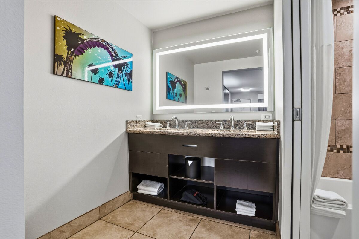 A modern bathroom with a dark vanity, a large mirror, and artwork on the wall.