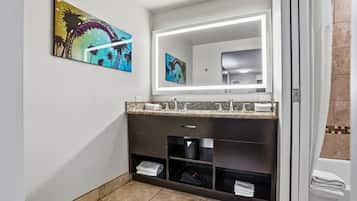 A modern bathroom with a dark vanity, a large mirror, and artwork on the wall.