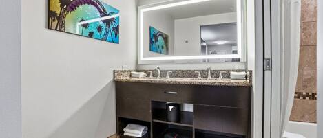 Un baño moderno con tocador oscuro, un espejo grande y una obra de arte en la pared.