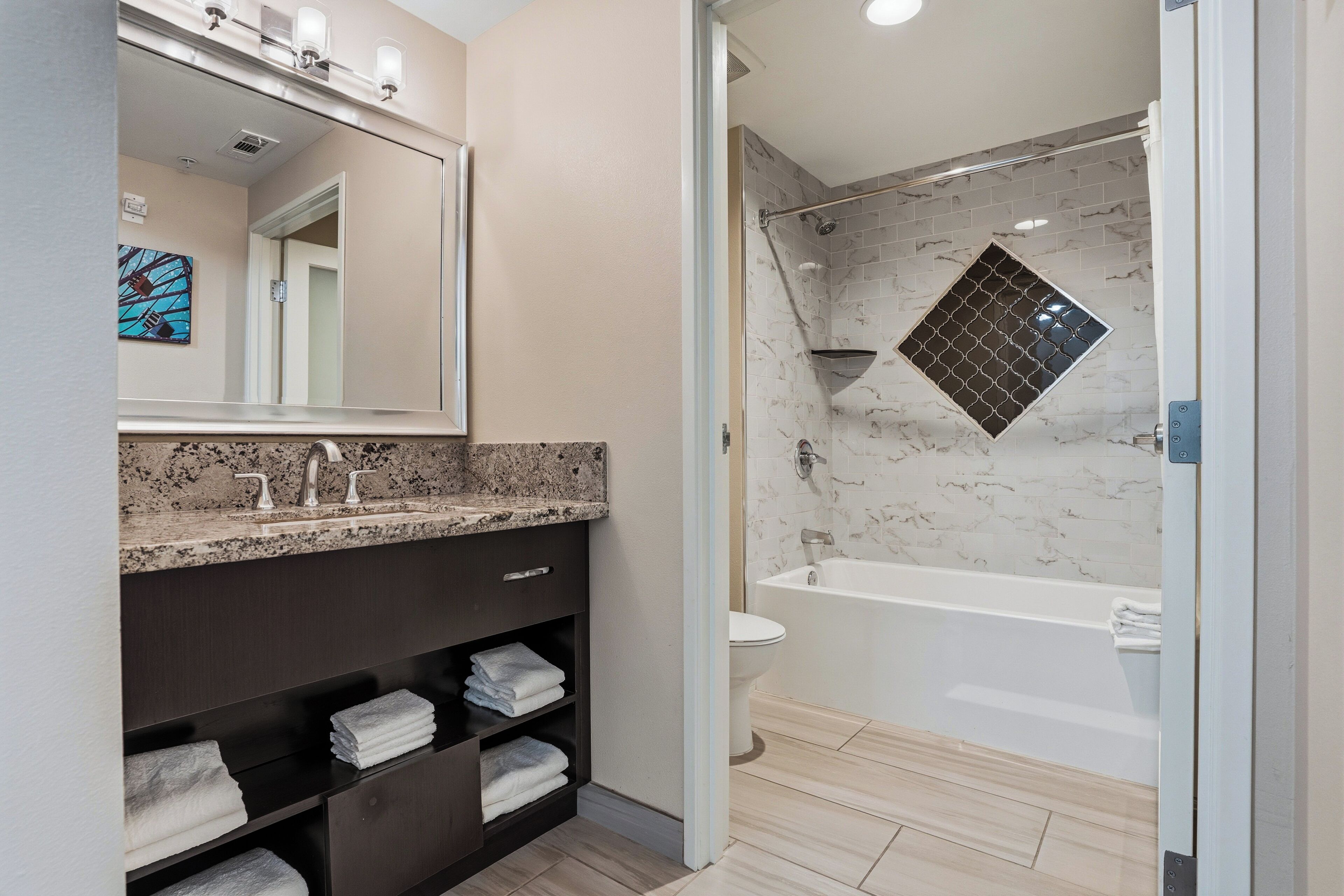 A modern bathroom with a granite countertop, a dark wooden vanity, a glass shower enclosure, and a marble-tiled shower wall.