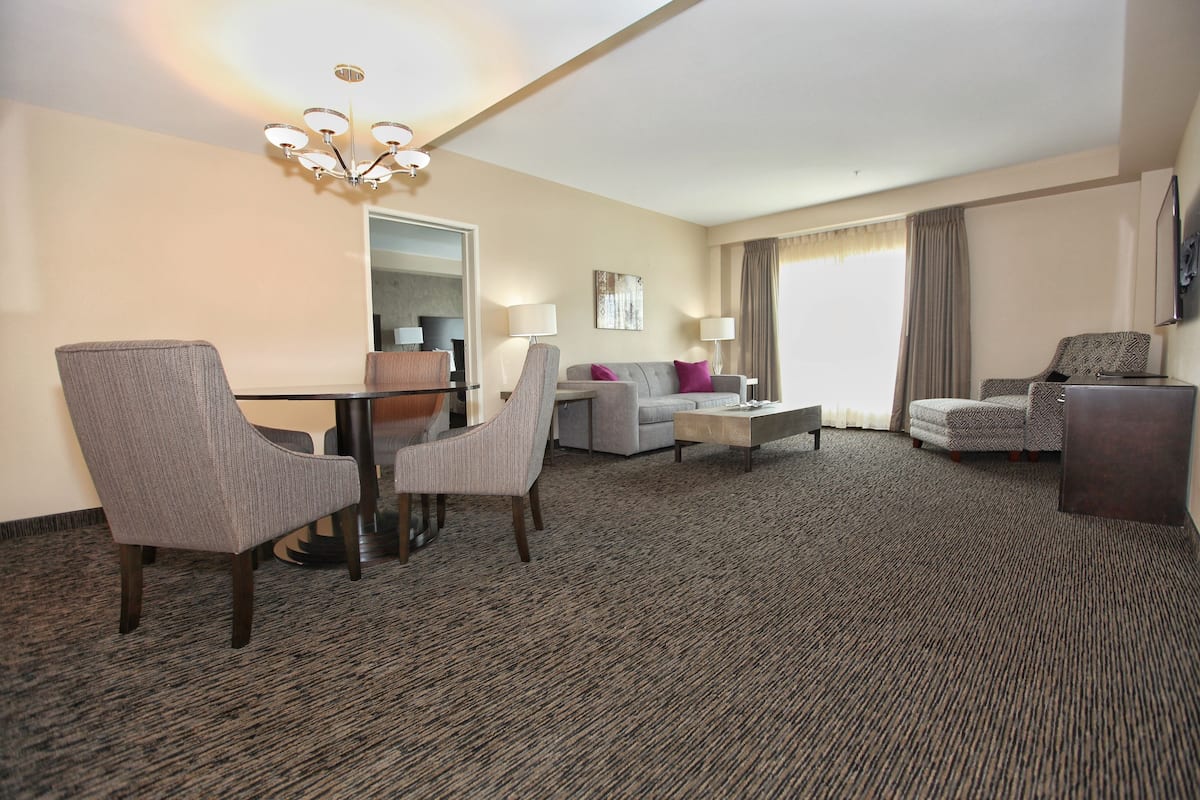 Une chambre d’hôtel avec un sol recouvert de moquette, une table à manger avec des chaises, un canapé, une table basse et un téléviseur fixé au mur.