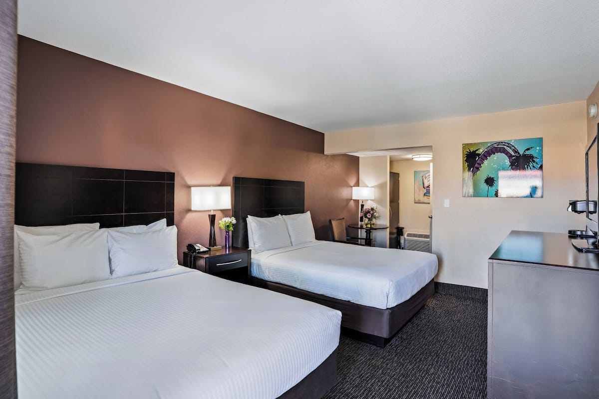 Une chambre d’hôtel avec deux lits, un bureau, une chaise, une lampe et un tableau au mur.
