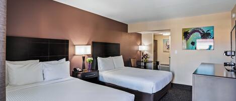 Quarto de hotel com duas camas, uma escrivaninha, uma cadeira, um abajur e um quadro na parede.