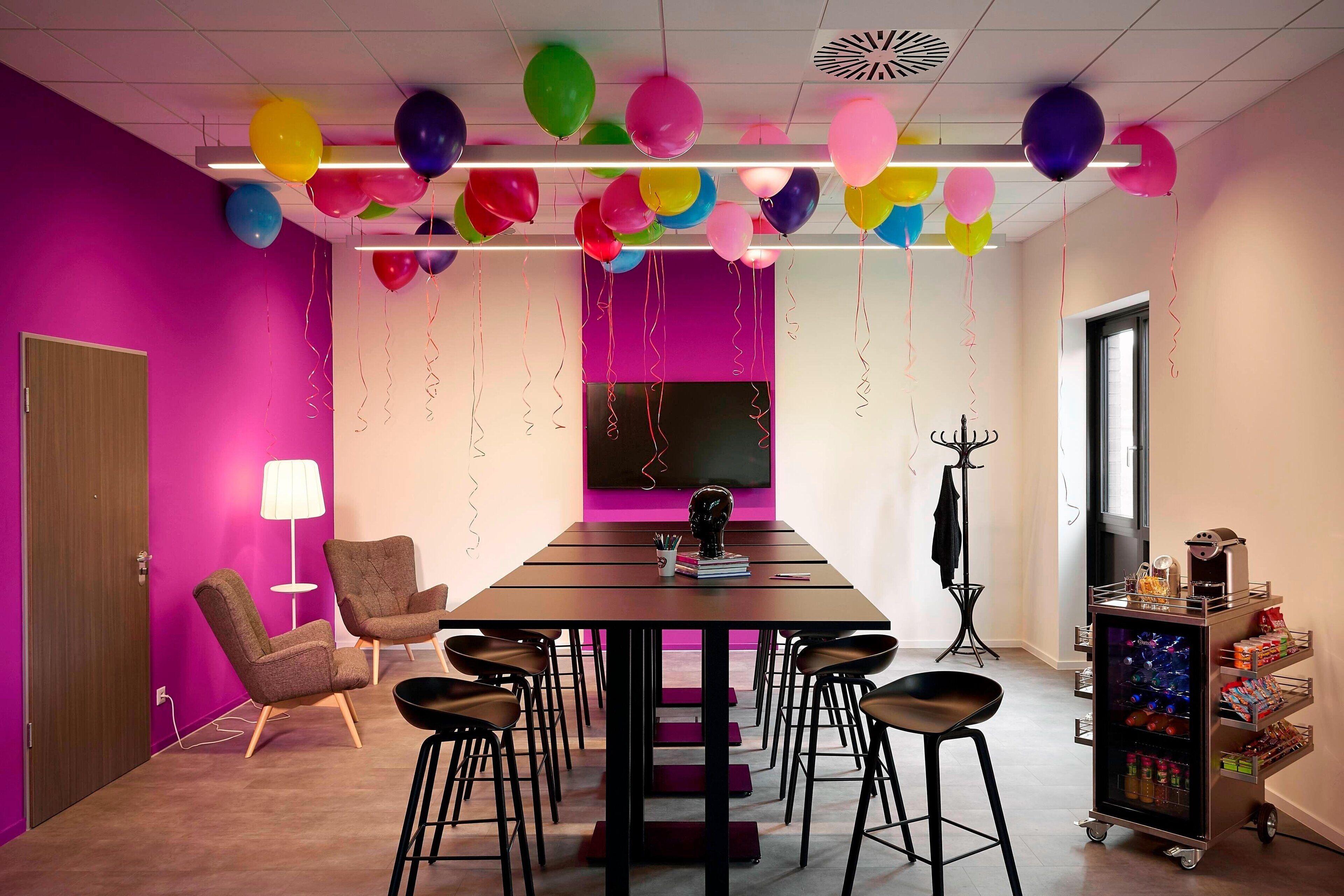 Une salle de conférence avec une longue table, de nombreuses chaises et des ballons de couleurs vives.