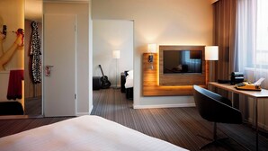 Een moderne hotelkamer met een groot bed, een bureau met een lamp, een televisie en een gitaar.