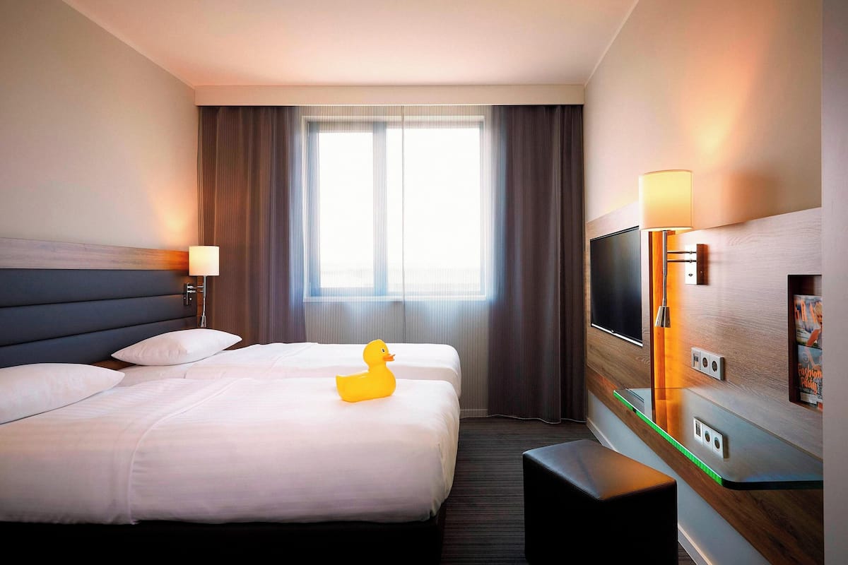 Habitación de hotel con dos camas, un televisor de pantalla plana, un escritorio y una ventana con cortinas.