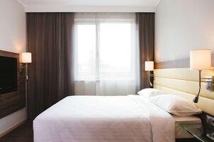 Habitación de hotel con una cama grande, dos lámparas de noche, un televisor de pantalla plana y una ventana con cortinas.