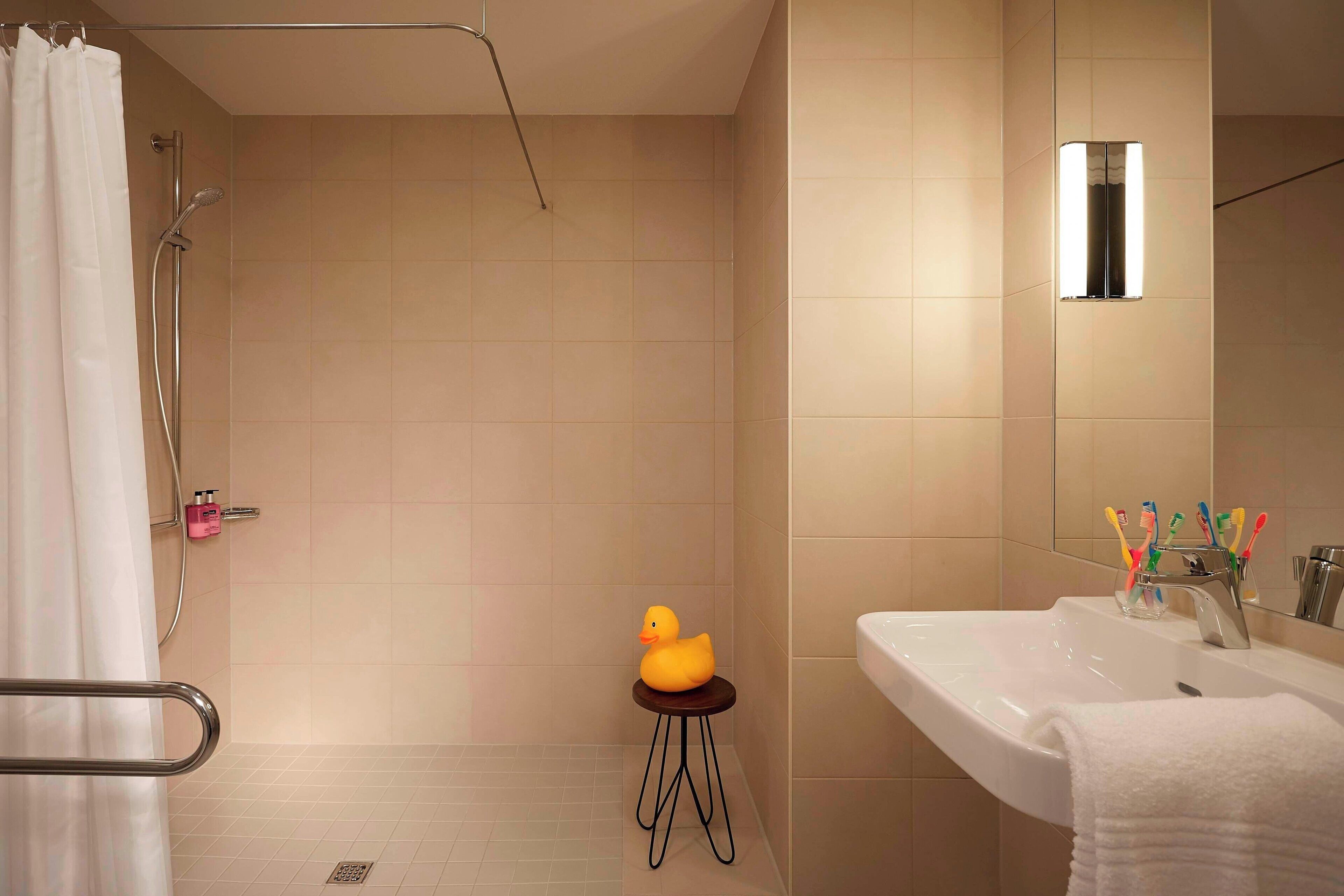 A bathroom with a shower, a sink with a mirror, and a small stool with a rubber duck.