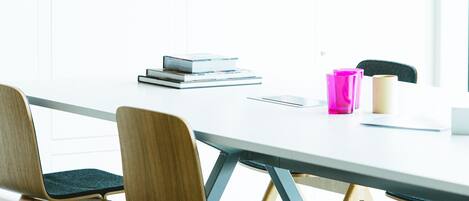 A modern meeting room with a white table, wooden chairs, and a bookshelf with various items.