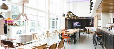 Un restaurant moderne avec des tables et des chaises en verre, un bar avec des tabourets et un grand écran de télévision.