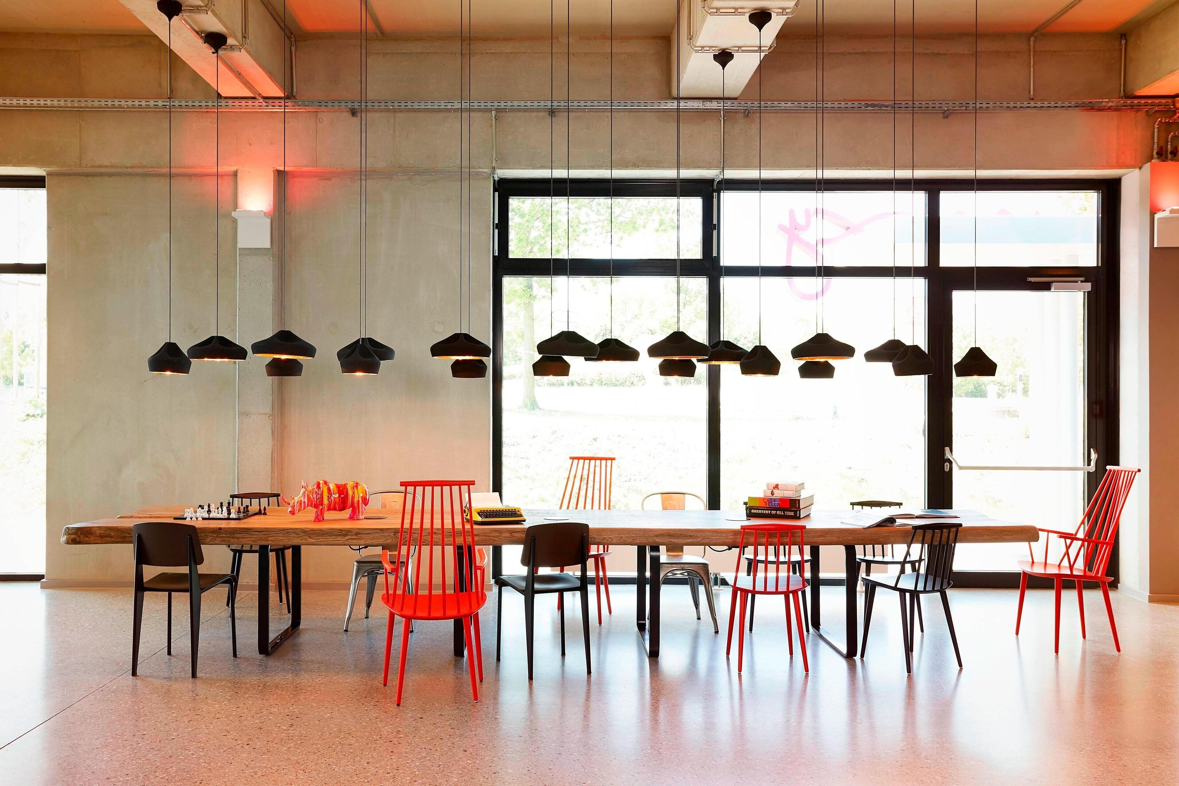 Un comedor moderno con una larga mesa de madera, sillas rojas y negras, y lámparas colgantes.
