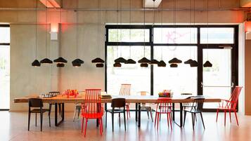 Un comedor moderno con una larga mesa de madera, sillas rojas y negras, y lámparas colgantes.