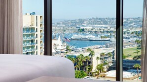 Une chambre d’hôtel dotée d’une grande fenêtre donnant sur un port de plaisance avec des bateaux et sur le paysage urbain.