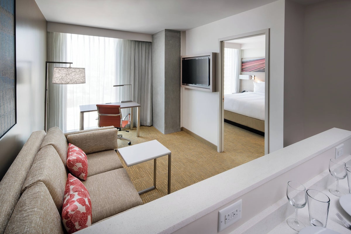 Una habitación de hotel moderna con sofá, una mesita, televisor y cama.