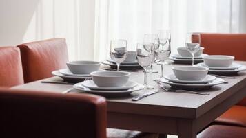 A dining table set with white bowls, plates, and wine glasses, surrounded by red leather chairs.