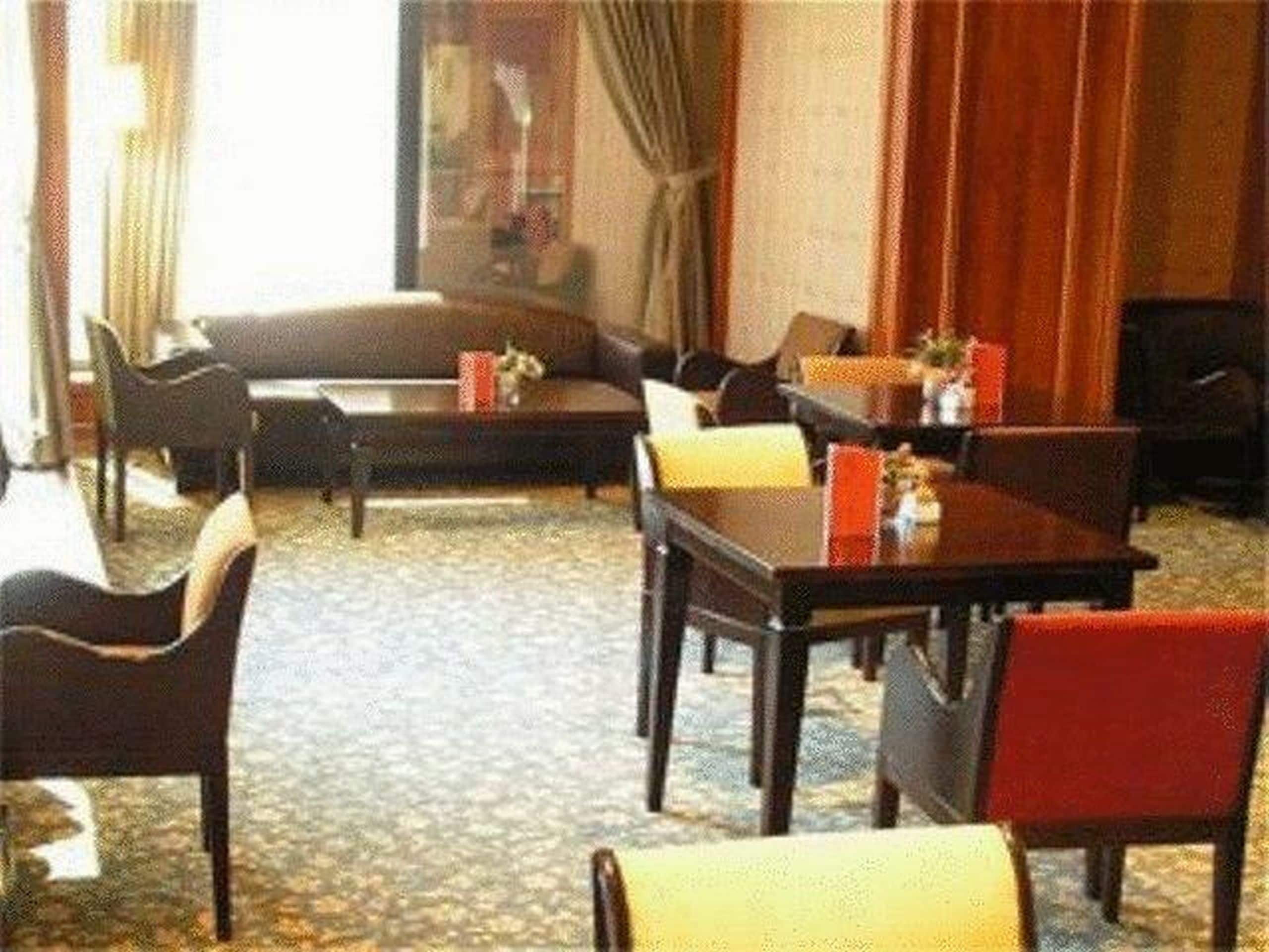 A hotel room with a sofa, dining table, chairs, and a carpeted floor.