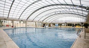 Piscina interior com teto de vidro, pistas demarcadas e espreguiçadeiras.