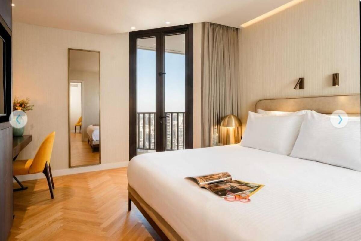 A hotel room with a large bed, a desk with a chair, a mirror, and a view of the outdoors.