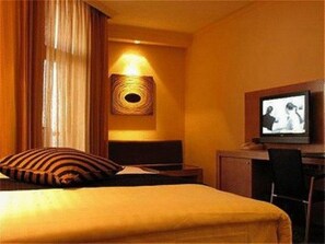 Quarto de hotel com cama, televisão, escrivaninha e uma cadeira.