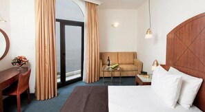A hotel room with a bed, a sofa, a desk, a chair, a small table, and a view through a large window. - Vert Jerusalem (Jerusalem)