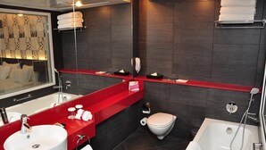 Ein modernes Badezimmer mit einer roten Ablage, einem weißen Waschbecken, einer Badewanne und einem WC.