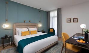 A hotel room with a bed, bedside tables, a desk, a chair, and a window with curtains.