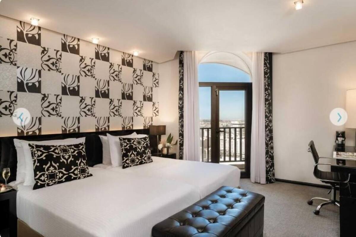 A hotel room with a large bed, a desk, a chair, a window with a view, and a balcony.