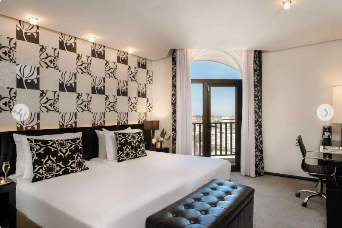 Ein Hotelzimmer mit einem großen Bett, einem Schreibtisch, einem Stuhl, einem Fenster mit Blick und einem Balkon.