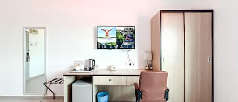 A hotel room with a desk, a chair, a wardrobe, a TV mounted on the wall, and a small trash bin.