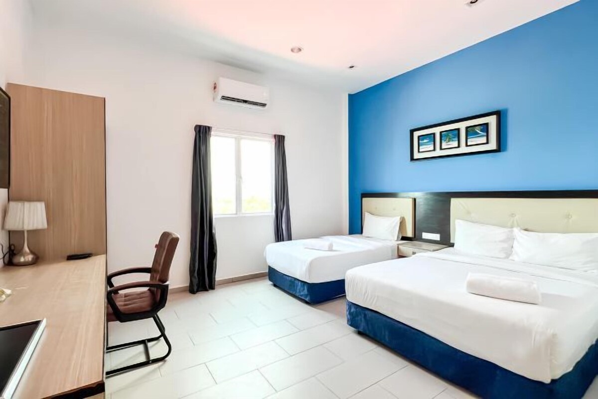 A hotel room with two beds, a desk, a chair, a window with curtains, and a wall-mounted air conditioner.