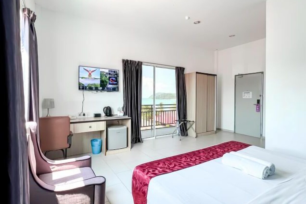 Quarto de hotel com cama, escrivaninha, cadeira, televisão e varanda com cortinas.