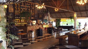 Un restaurante con piso a cuadros, una zona de bar con estantes llenos de botellas y un techo de paja.