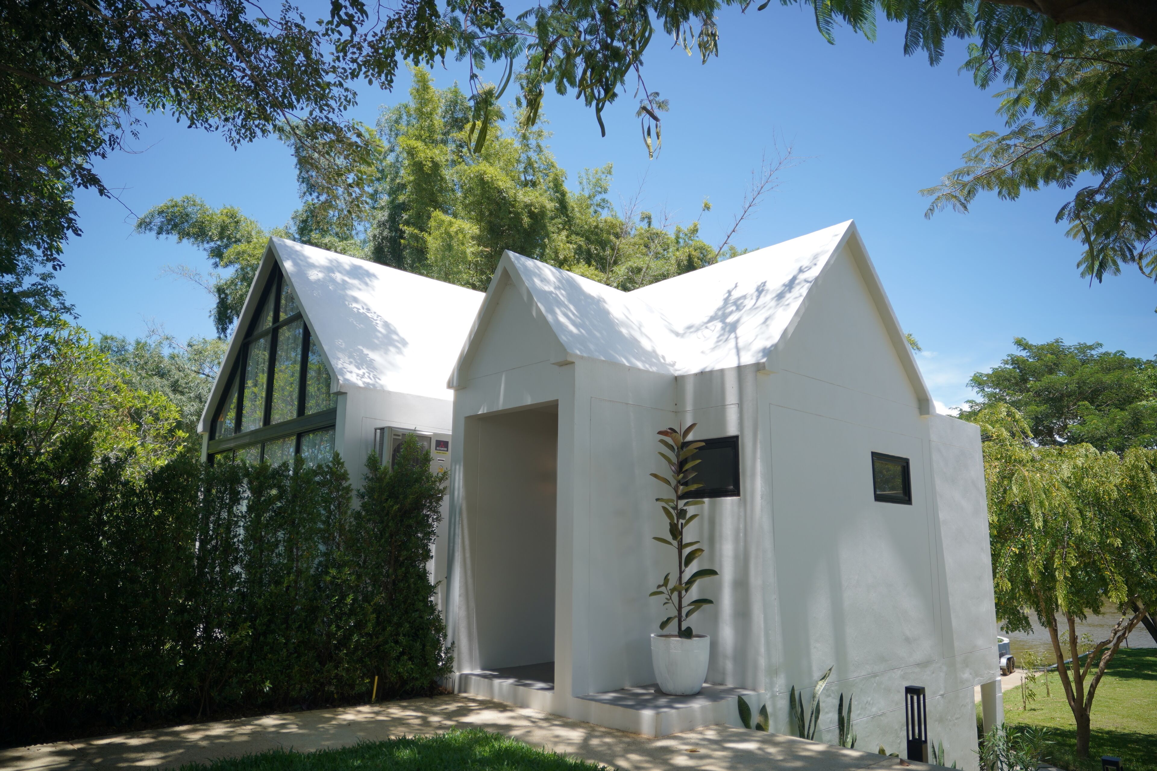 Un edificio moderno con techo triangular y amplias ventanas, rodeado de abundante vegetación.