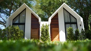 Dos edificios modernos, blancos y de forma triangular, con detalles de madera y ventanas amplias, rodeados de exuberante vegetación.