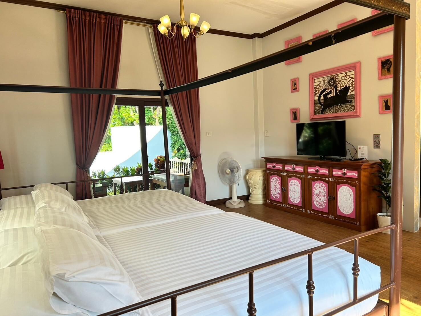 A bedroom with a large bed, a TV, a fan, and a view of the outdoors.
