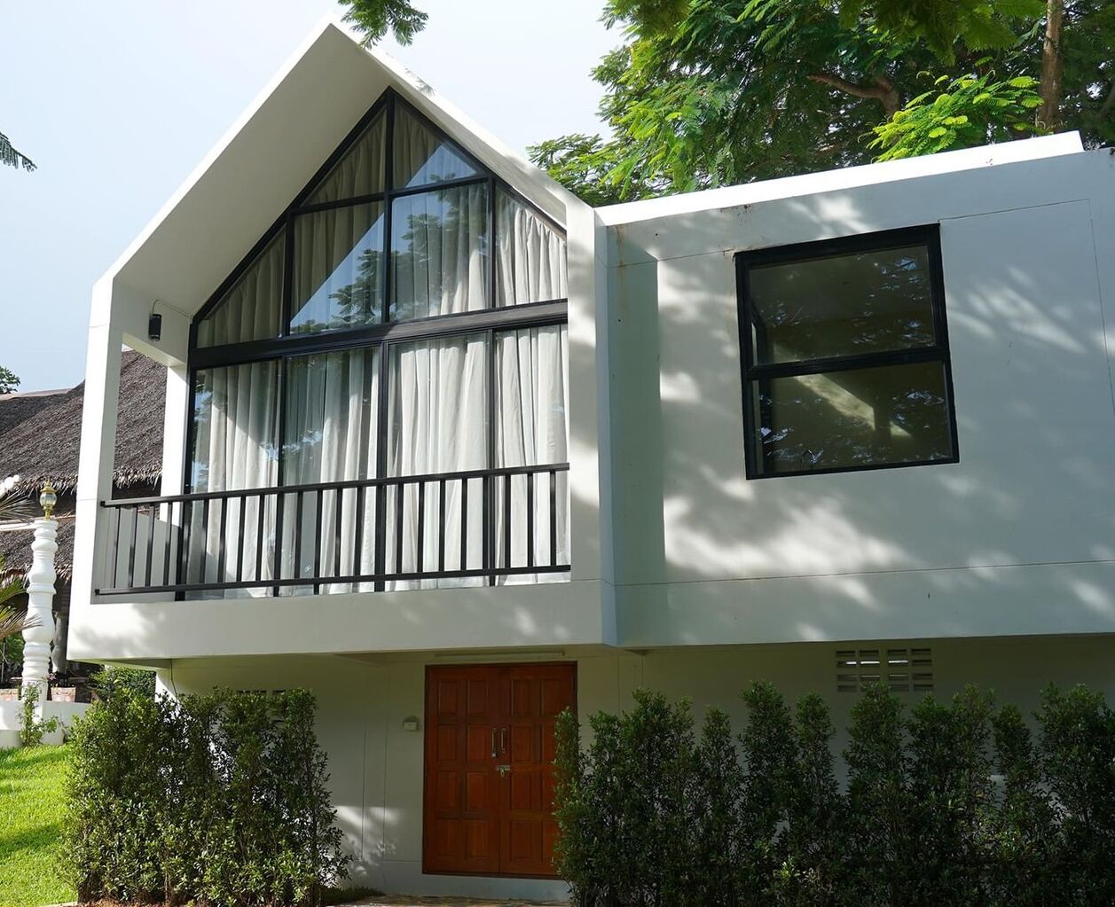 A modern two-story building with large windows, a balcony, and a wooden door.